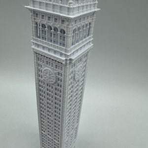 May include: A white 3D printed model of a tall building with intricate details, including a clock face and many windows.