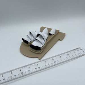 May include: A white model of the Sydney Opera House on a brown base. The model is approximately 6 inches long.