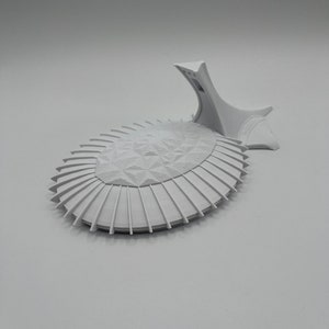 May include: A white 3D printed model of a futuristic building with a geometric design. The model is on a white background.
