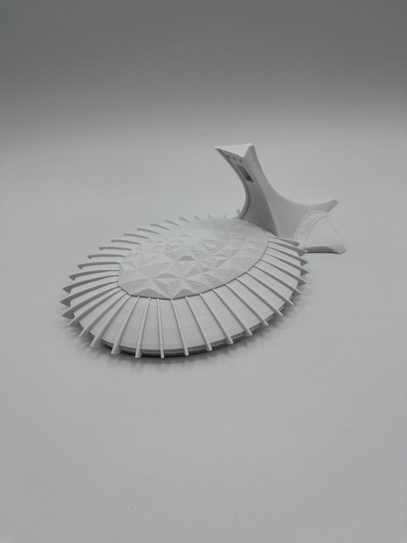 May include: A white 3D printed model of a futuristic building with a geometric design. The model is on a white background.