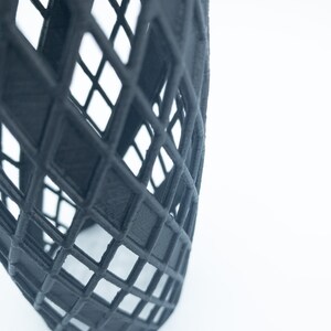 May include: A black, 3D printed, geometric sculpture with a grid pattern. The sculpture is cylindrical and has a twisted design.
