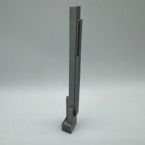 Op de afbeelding: Een grijs 3D-geprint model van een hoog wolkenkrabbergebouw.