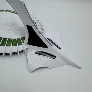Puede incluir: Maqueta arquitect&oacute;nica impresa en 3D, blanca, con base circular y detalles verdes, y una estructura curva en forma de ala. El dise&ntilde;o presenta detalles intrincados y una est&eacute;tica moderna.