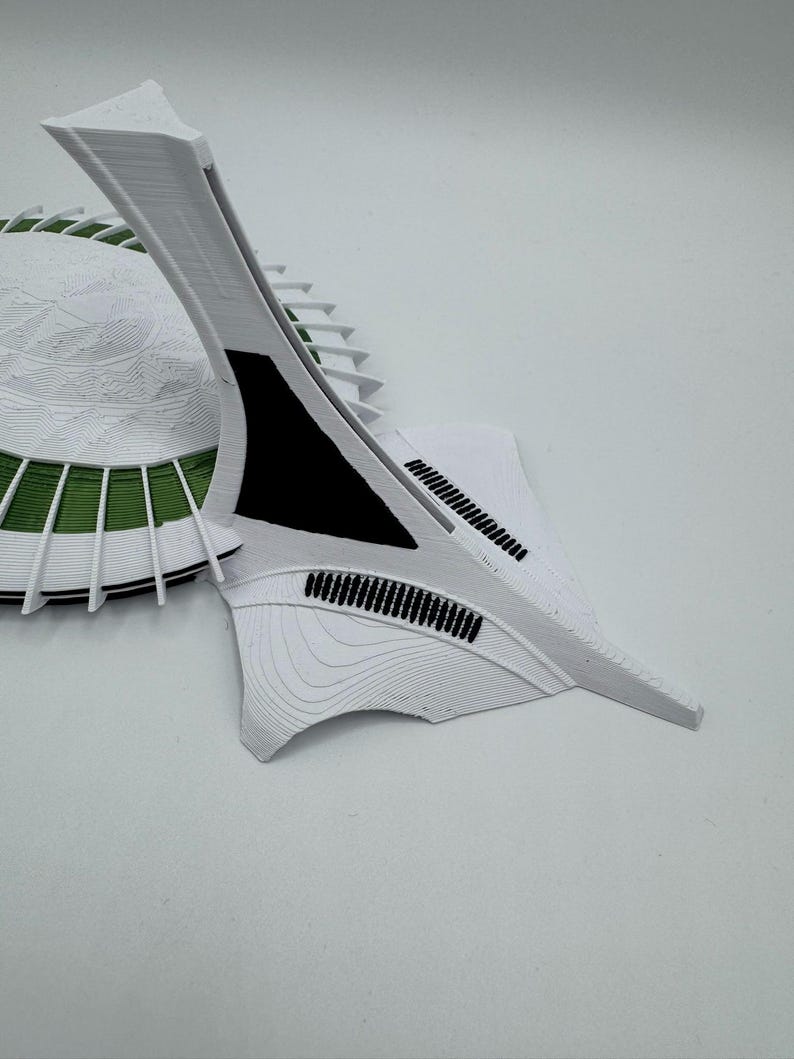 Puede incluir: Maqueta arquitect&oacute;nica impresa en 3D, blanca, con base circular y detalles verdes, y una estructura curva en forma de ala. El dise&ntilde;o presenta detalles intrincados y una est&eacute;tica moderna.