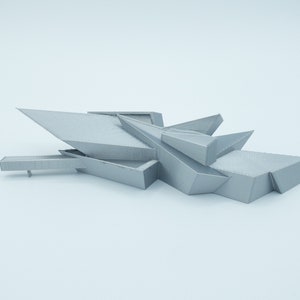 May include: A 3D printed model of a modern building with a geometric design. The model is made of a light gray plastic and has a sharp, angular shape.