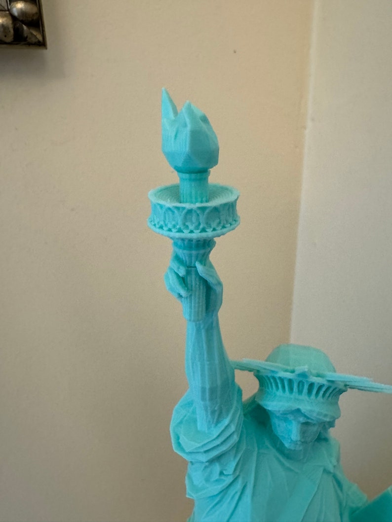 May include: A teal blue 3D printed statue of the Statue of Liberty holding a torch in her right hand.
