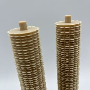 May include: Two beige, cylindrical, decorative items with a textured, scalloped design. The items are made of a lightweight material and have a smooth, rounded top.