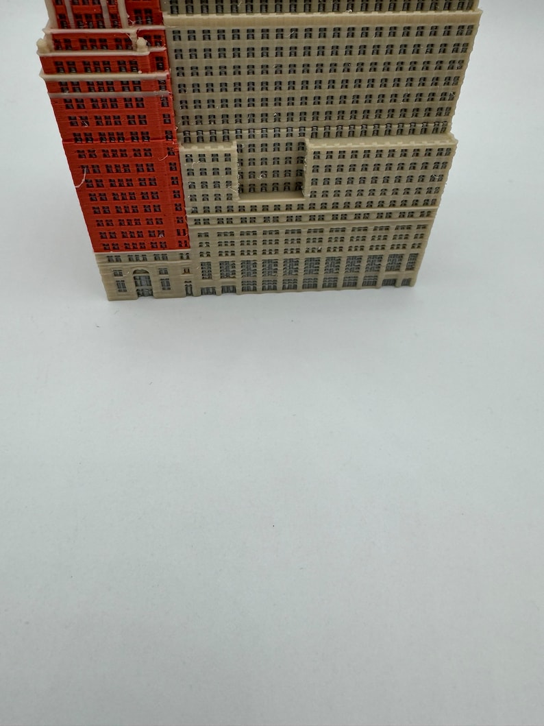 May include: A miniature model of a tall building with a red brick facade and a beige facade with many windows.