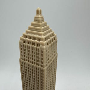Puede incluir: Un modelo de rascacielos impreso en 3D de color beige con una fachada detallada y un techo piramidal.