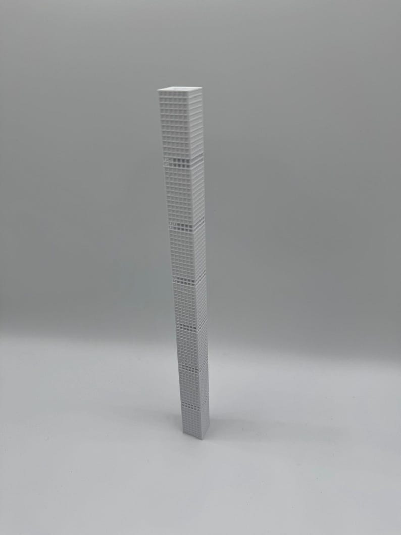 May include: A tall, slender, grey model of a skyscraper. The building has a rectangular shape with many windows and a flat roof. The model is standing upright against a plain grey background.