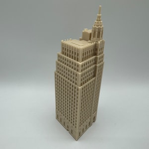 Pu&ograve; includere: Un modello di grattacielo alto stampato in 3D di colore beige con un tetto a punta e molte finestre.