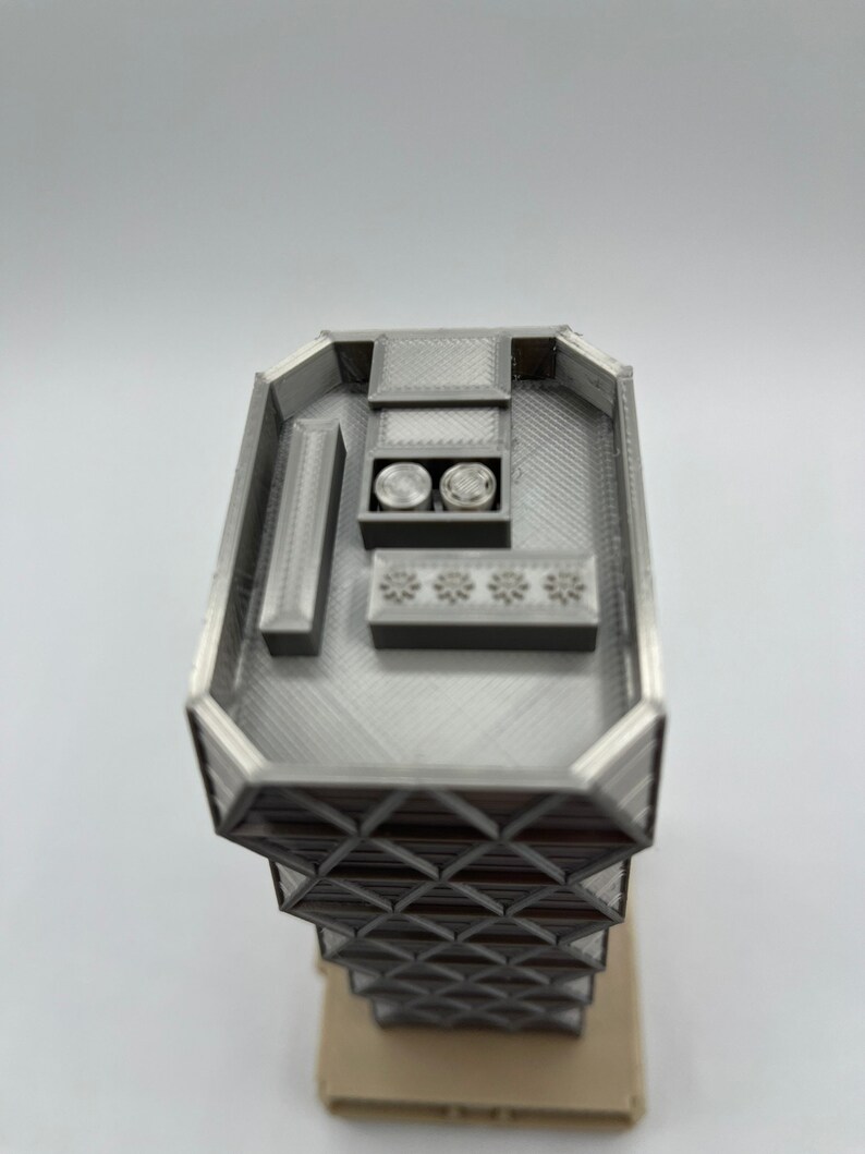May include: A 3D printed model of a modern skyscraper with a detailed rooftop and a geometric facade.