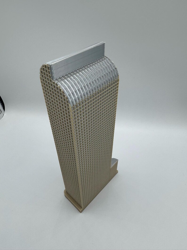 May include: A beige, 3D-printed architectural model of a skyscraper. The building has a rectangular base and a tall, grid-like structure. The top of the building has a curved design with a silver-colored accent.
