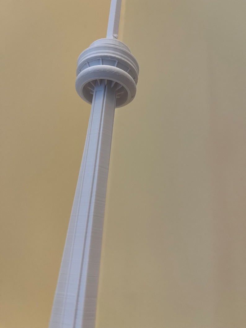 May include: A light gray model of the CN Tower, a tall structure with a distinctive observation deck and antenna. The tower's design includes a central core and a series of circular platforms. The model is set against a plain background.