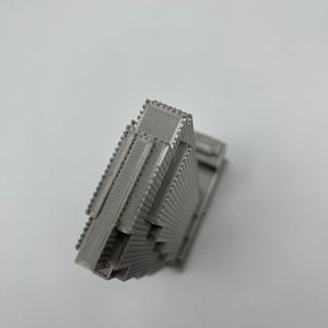 May include: A 3D printed model of a skyscraper, with a detailed facade and a textured surface. The model is made of a silver-colored material.