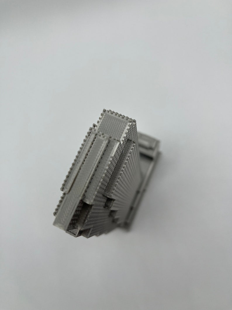 May include: A 3D printed model of a skyscraper, with a detailed facade and a textured surface. The model is made of a silver-colored material.