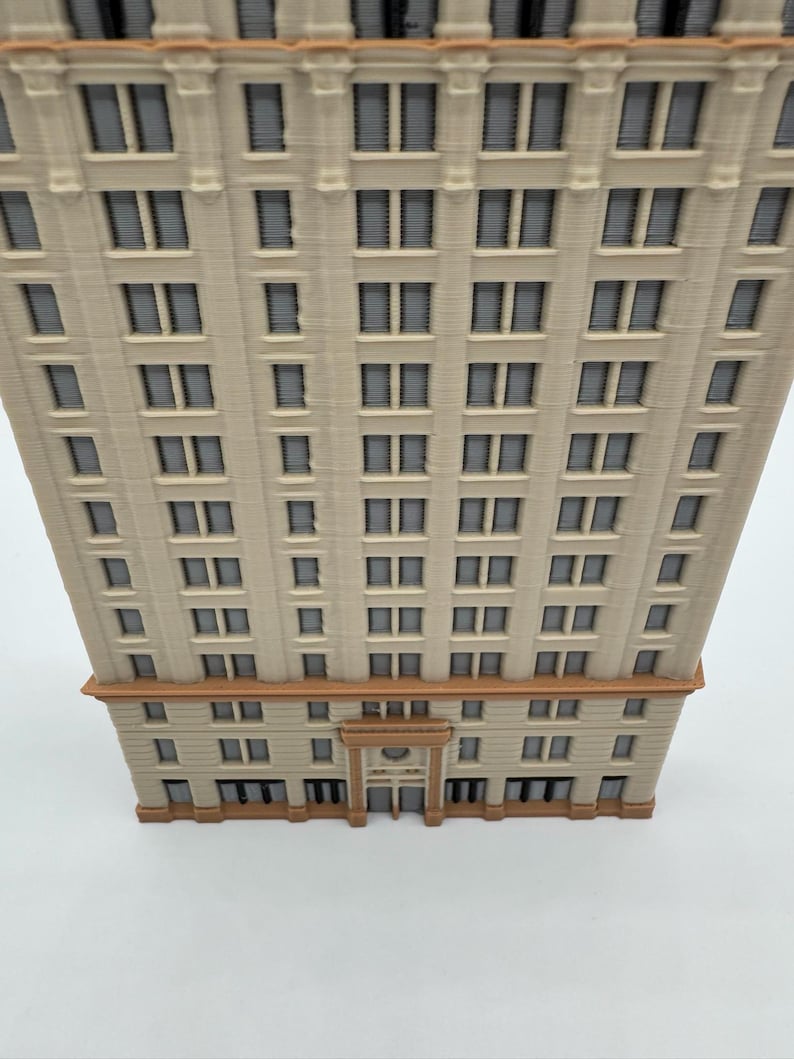 May include: A detailed model of a multi-story building with numerous windows. The building has a beige facade with brown accents at the base and top. The windows are dark, and the overall design suggests a classic architectural style.
