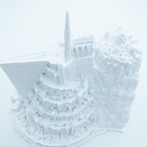 May include: A white 3D printed model of a fantasy castle with a tall tower and intricate details.