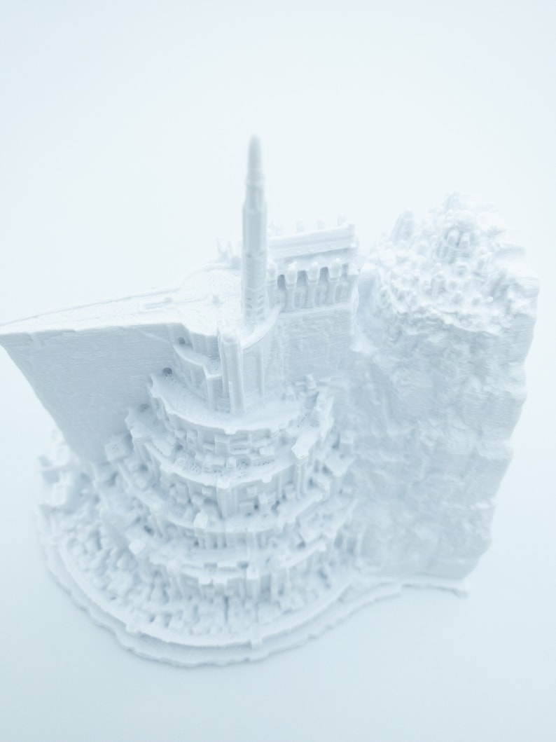 May include: A white 3D printed model of a fantasy castle with a tall tower and intricate details.