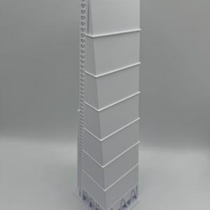 May include: A tall, white, architectural model of a grain silo or industrial structure. The model has a rectangular shape with multiple stacked sections and a ladder running along one side. The base is a triangular shape.