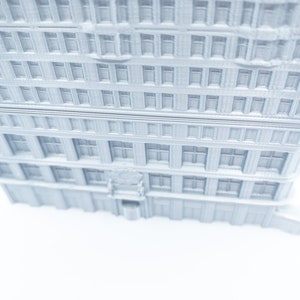 Puede incluir: Un modelo 3D impreso en blanco de un edificio alto con muchas ventanas. El edificio est&aacute; sobre un fondo blanco.