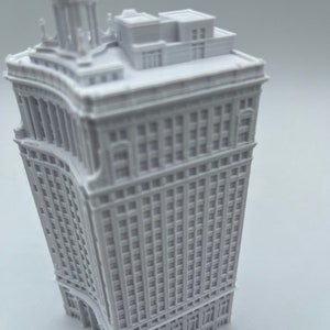 Op de afbeelding: Een wit 3D-geprint model van een hoog gebouw met een gebogen gevel en een gedetailleerd dak.