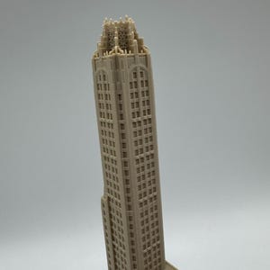 May include: A beige, miniature skyscraper model with intricate architectural details. The building has numerous windows and a detailed crown. The model is a representation of a famous building, perfect for display or as a collectible item.