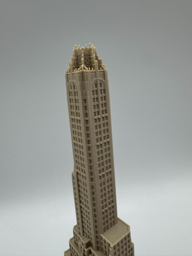 May include: A beige, miniature skyscraper model with intricate architectural details. The building has numerous windows and a detailed crown. The model is a representation of a famous building, perfect for display or as a collectible item.