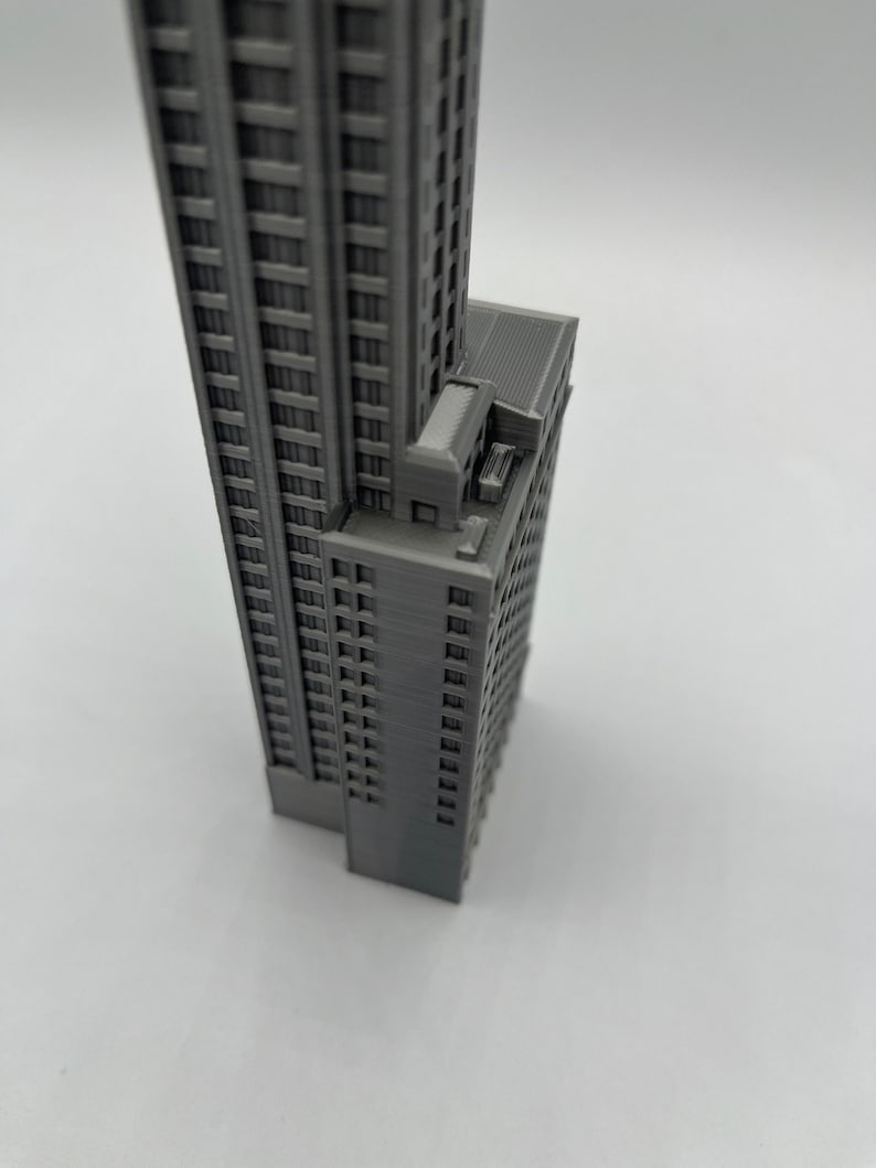 May include: A gray 3D printed model of a tall building with many windows. The building has a flat roof and a small, rectangular structure on the side.