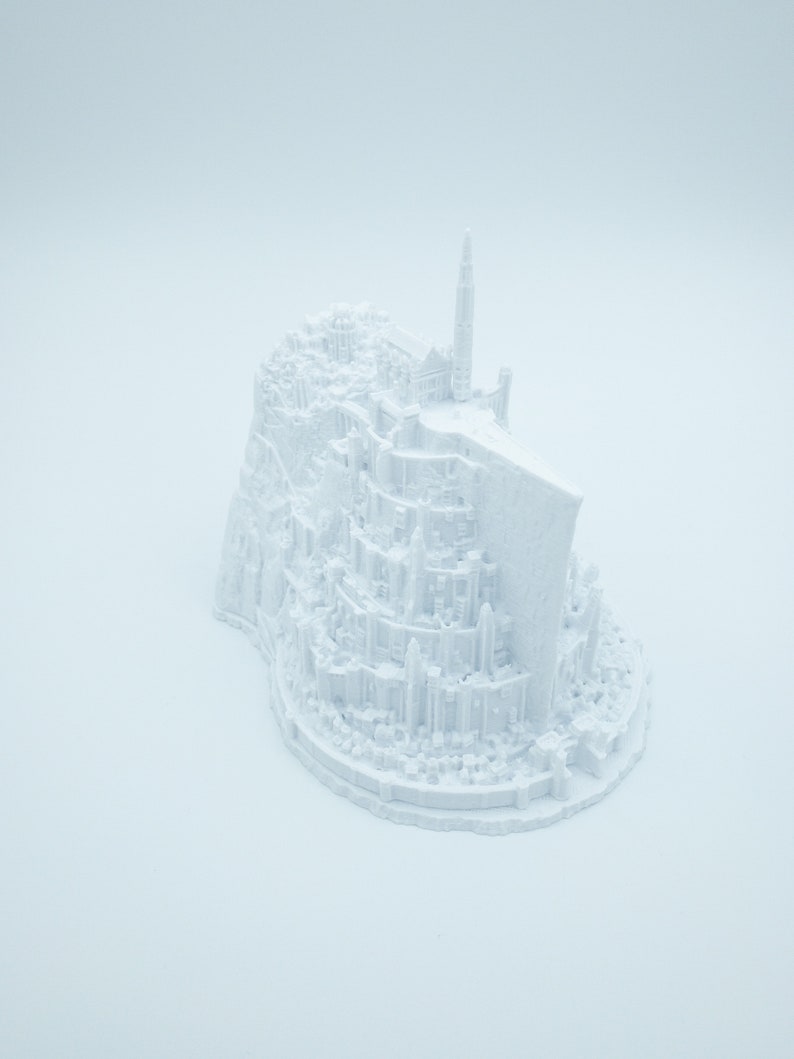 May include: A white 3D printed model of a fantasy city with a tall tower, resembling a fictional castle.