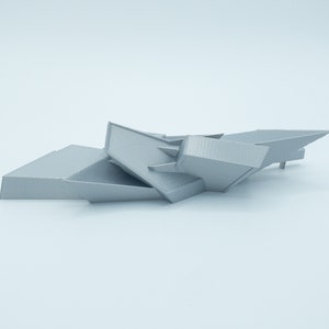 May include: A 3D printed model of a geometric abstract sculpture. The sculpture is made of gray plastic and has a sharp, angular design.