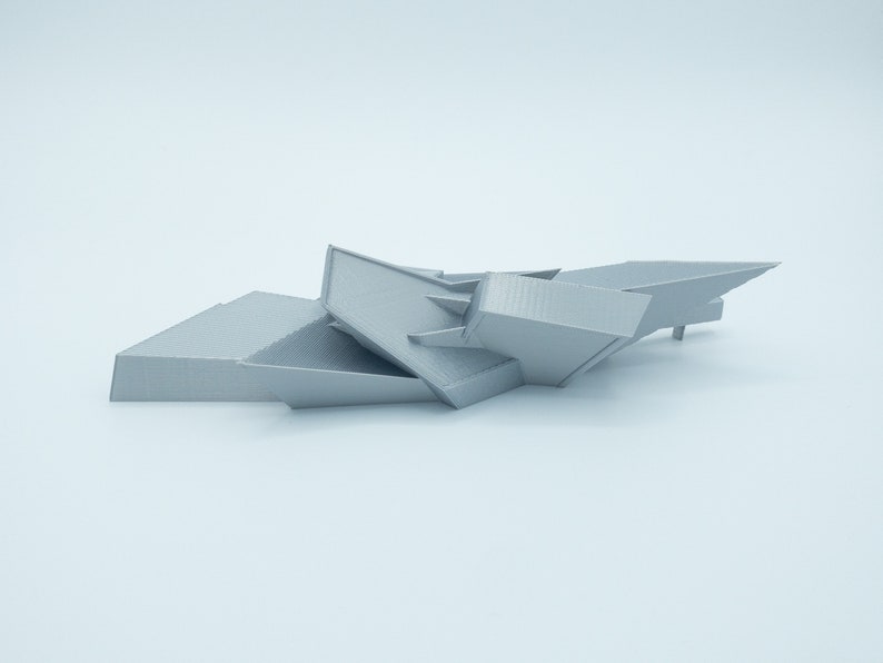 May include: A 3D printed model of a geometric abstract sculpture. The sculpture is made of gray plastic and has a sharp, angular design.