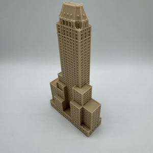 Może przedstawiać: Beżowy miniaturowy model wieżowca z szczeg&oacute;łowymi elementami architektonicznymi. Budynek ma wielopoziomową konstrukcję z licznymi oknami i szczeg&oacute;łowym dachem. Model jest reprezentacją znanego budynku.