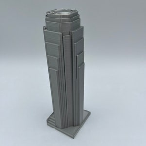 May include: A gray 3D printed model of a skyscraper with a detailed facade and a stepped base.