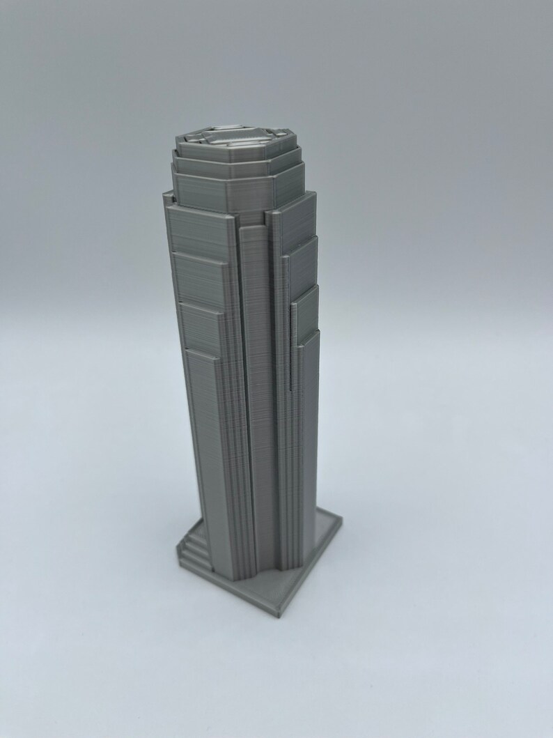 May include: A gray 3D printed model of a skyscraper with a detailed facade and a stepped base.