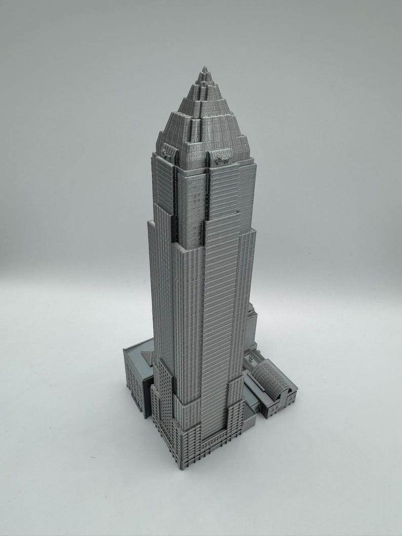 May include: A gray, 3D-printed model of a skyscraper. The building has a tiered design with a pointed top and detailed architectural features. The model is set against a plain white background.