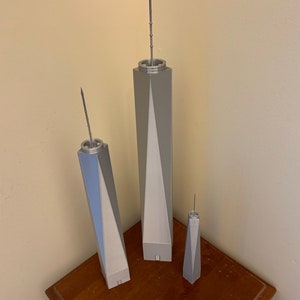May include: Three silver model skyscrapers of varying sizes, the tallest is about 10 inches tall, the middle is about 6 inches tall, and the smallest is about 4 inches tall. The models are on a wooden surface with a ruler.