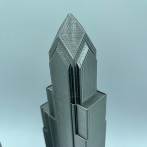 May include: A 3D printed model of a skyscraper with a pointed top and a textured surface.