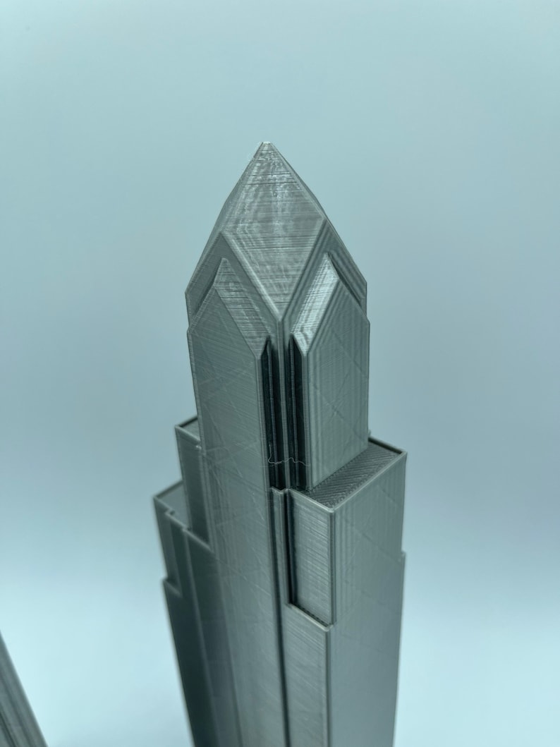 May include: A 3D printed model of a skyscraper with a pointed top and a textured surface.