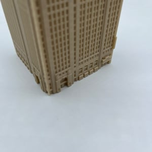 May include: A beige plastic model of a tall building with many windows. The model is detailed with small windows and a base.