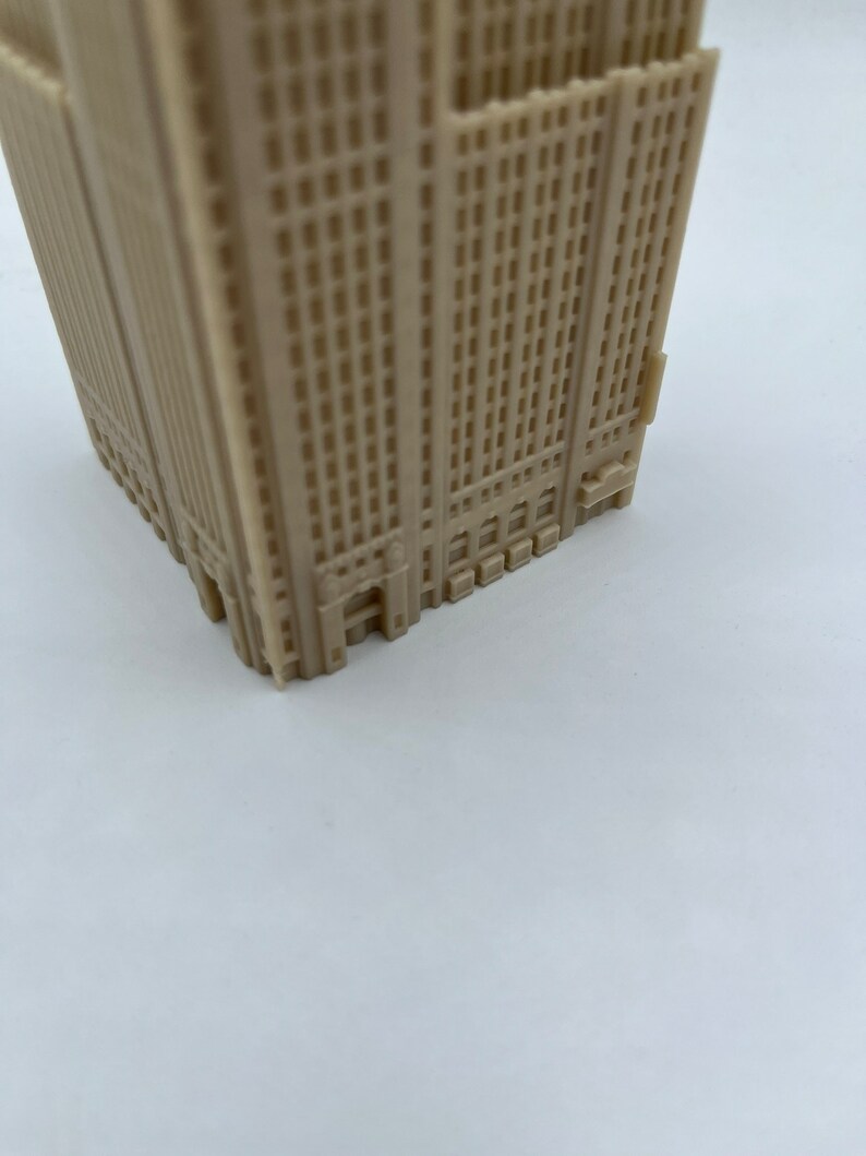 May include: A beige plastic model of a tall building with many windows. The model is detailed with small windows and a base.