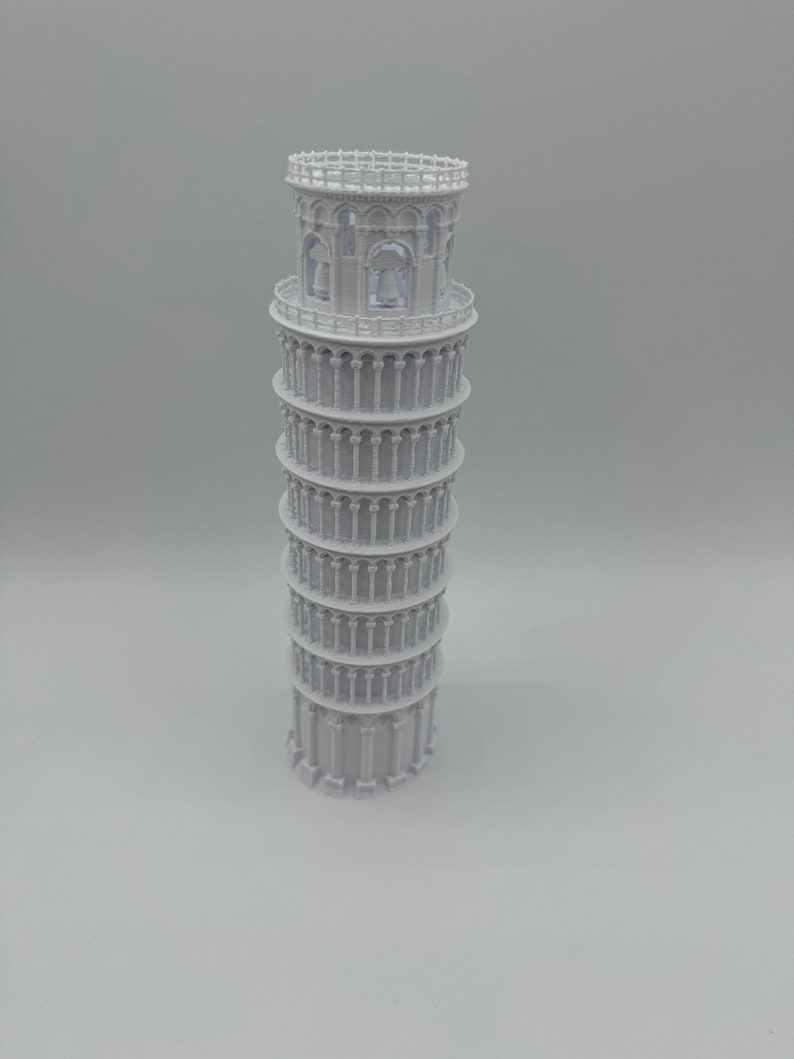 May include: A white 3D printed model of the Leaning Tower of Pisa. The model is detailed with arches and columns.