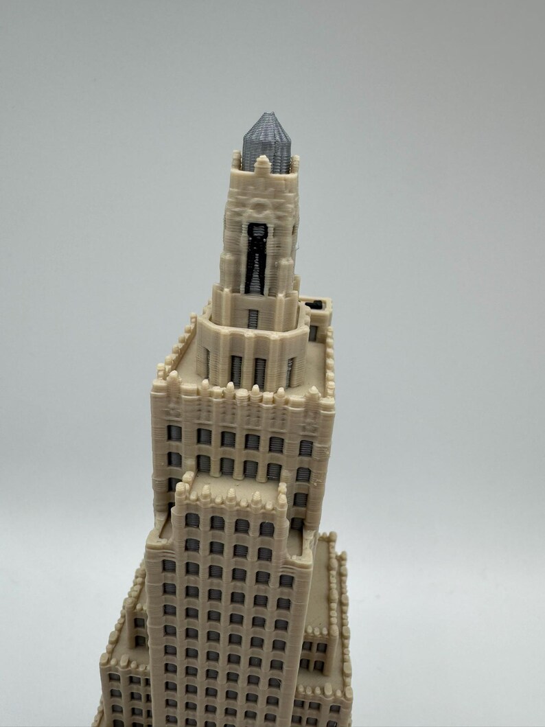 May include: A detailed, off-white miniature of a tall building with a gray, textured top. The building has many windows and architectural details, suggesting a skyscraper or historical structure. The model is likely 3D-printed.