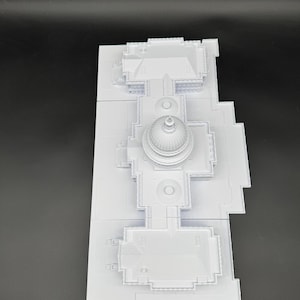 K&ouml;nnte beinhalten: Ein wei&szlig;es Architekturmodell eines Geb&auml;udes mit einer zentralen Kuppel und mehreren rechteckigen Abschnitten. Das Modell ist aus mehreren Teilen zusammengesetzt und zeigt detaillierte Merkmale wie Fenster und Dachlinien. Das Modell befindet sich auf einer dunklen Oberfl&auml;che.