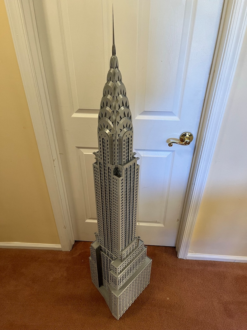 May include: A detailed model of the Chrysler Building in New York City, made of gray plastic. The model is tall and slender, with a pointed spire at the top. The building is decorated with intricate details, including windows, arches, and gargoyles.