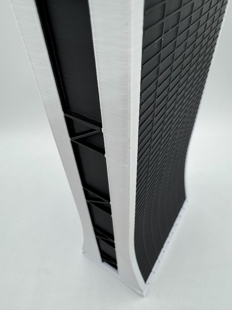 May include: A white and black 3D printed model of a tall building with a curved facade. The building has a grid pattern on the front and a white trim around the edges.