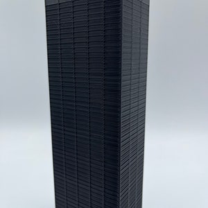 May include: A black 3D printed model of a skyscraper with a grid pattern on the facade.