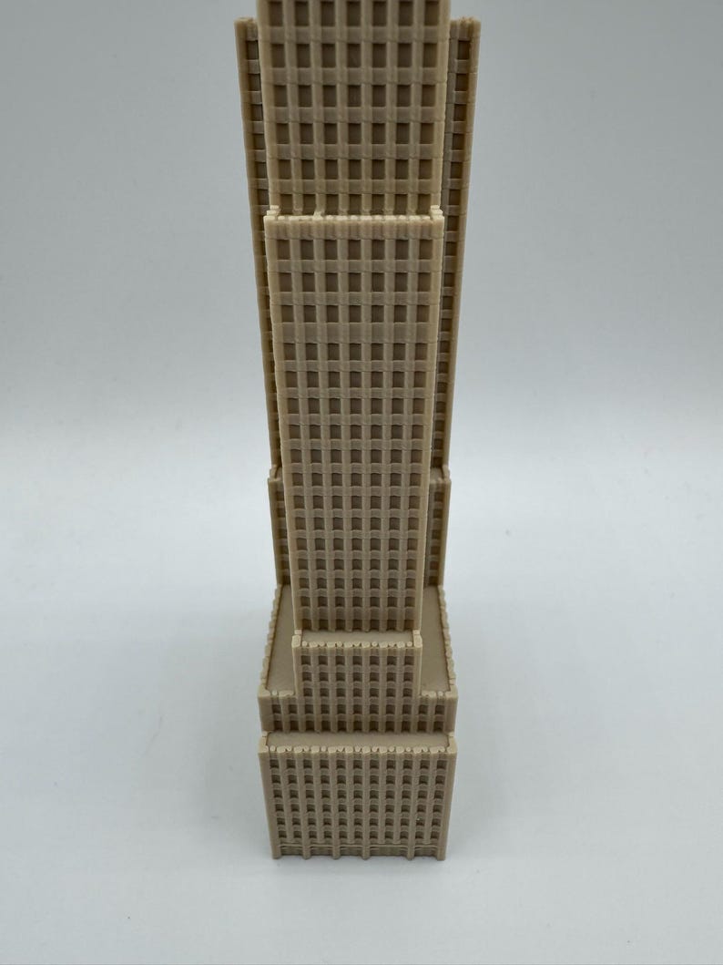 May include: A beige architectural model of a skyscraper. The building has a rectangular shape with multiple tiers and a grid-like pattern of windows. The model is made of a solid material and stands upright against a white background.