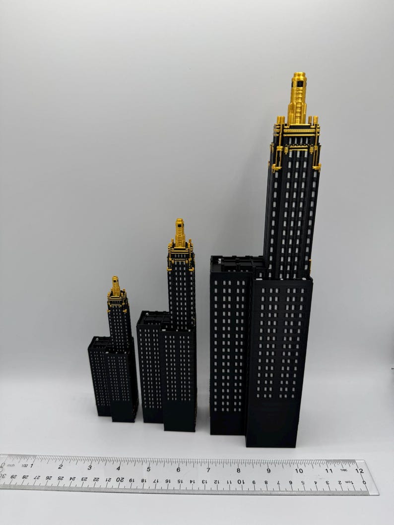 Op de afbeelding: Een verzameling zwarte miniatuur wolkenkrabbermodellen met goudkleurige toppen. De gebouwen vari&euml;ren in grootte en zijn in een groep gerangschikt. Een liniaal staat onderaan de afbeelding, met afmetingen in centimeters.