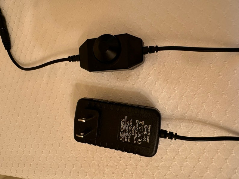 May include: A black AC adapter with a power cord and a black dimmer switch with a knob. The AC adapter has the text "AC/DC ADAPTOR MODEL AYD-1220 INPUT AC100-240V 50/60Hz OUTPUT DC12V 2A CE  MADE IN CHINA" printed on it.